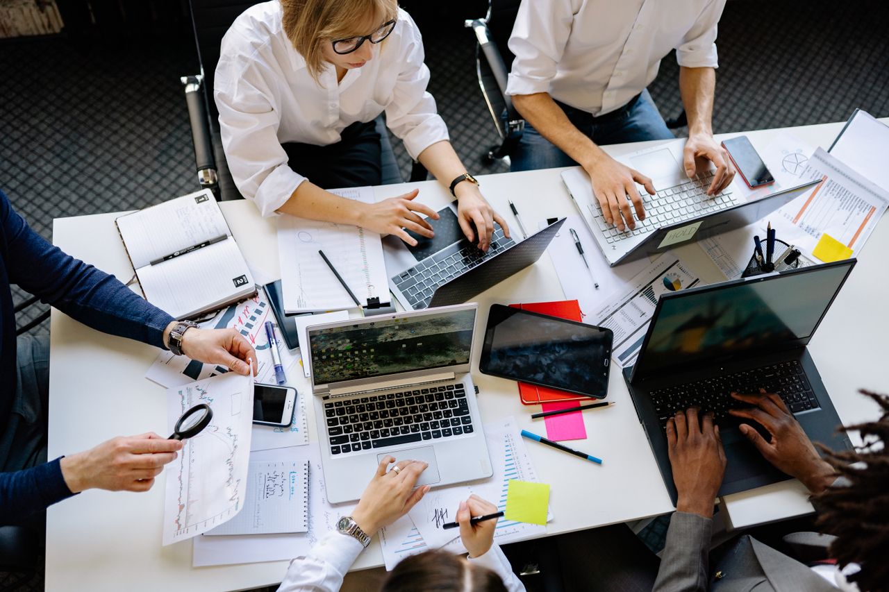 Vue plongeante d’une équipe d’entreprise travaillant ensemble avec des ordinateurs portables et des documents.